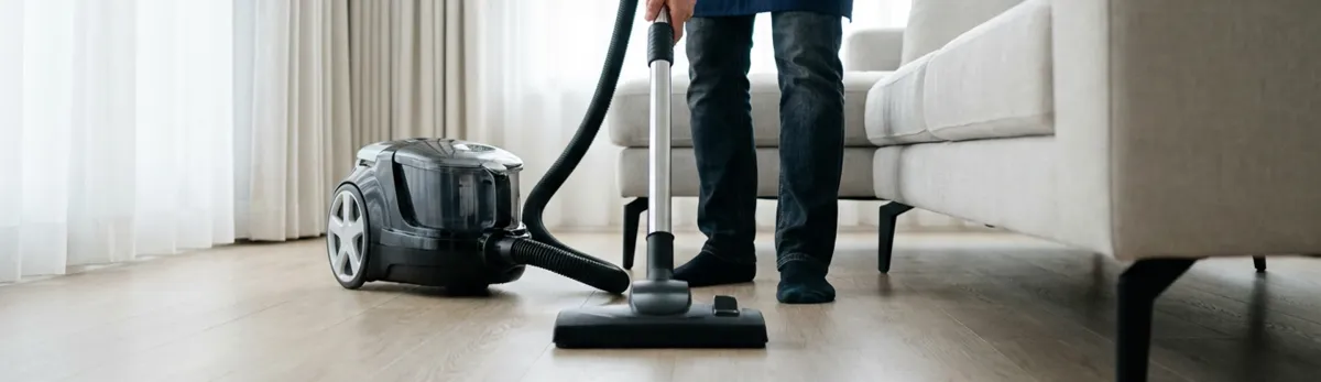 Professional house cleaner vacuuming a living room floor with a canister vacuum cleaner, Providence, RI.